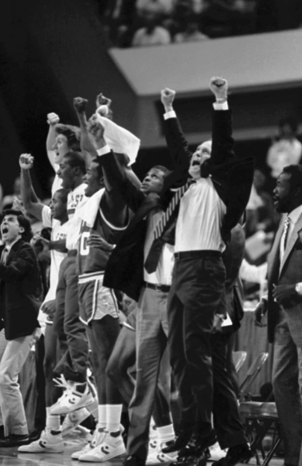 Louisiana State University coach Dale Brown, right, and team members on the sidelines raise...