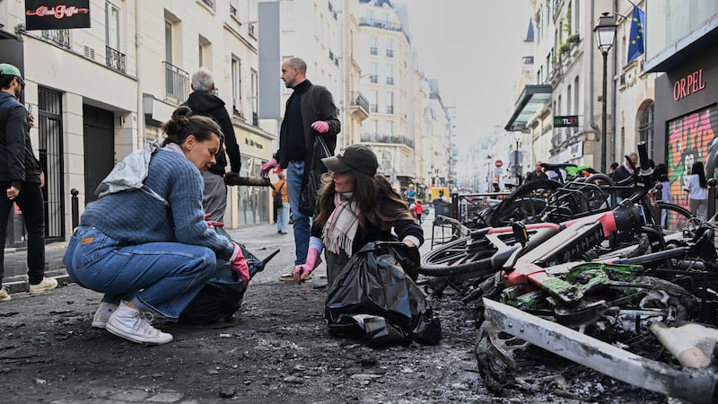 People clean up debris Sunday (Oct. 18) in a street next to burned bicycles, one day after a...